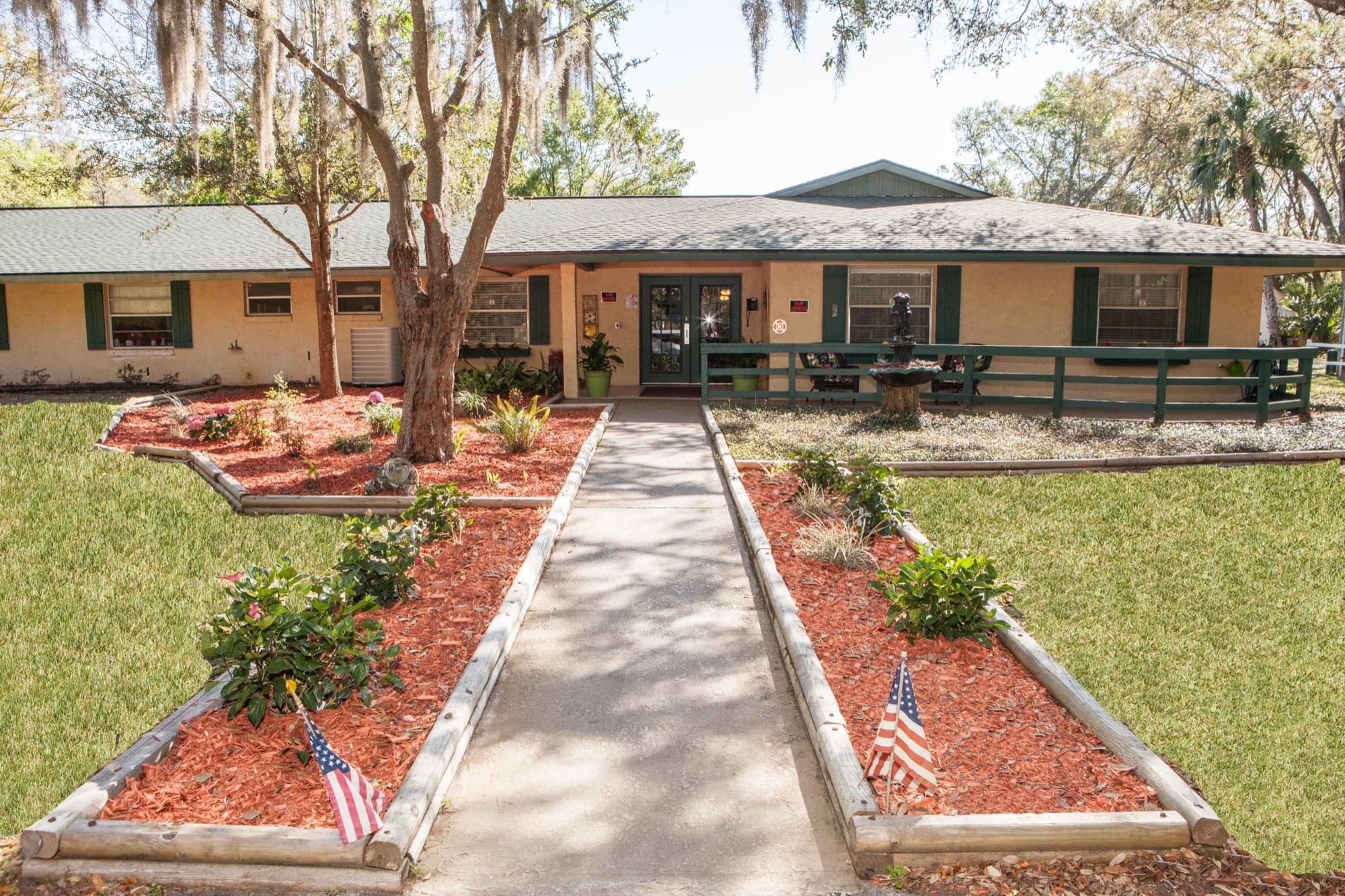 The Gardens of Crystal River beneath a live oak, with garden beds and a flag at the entrance